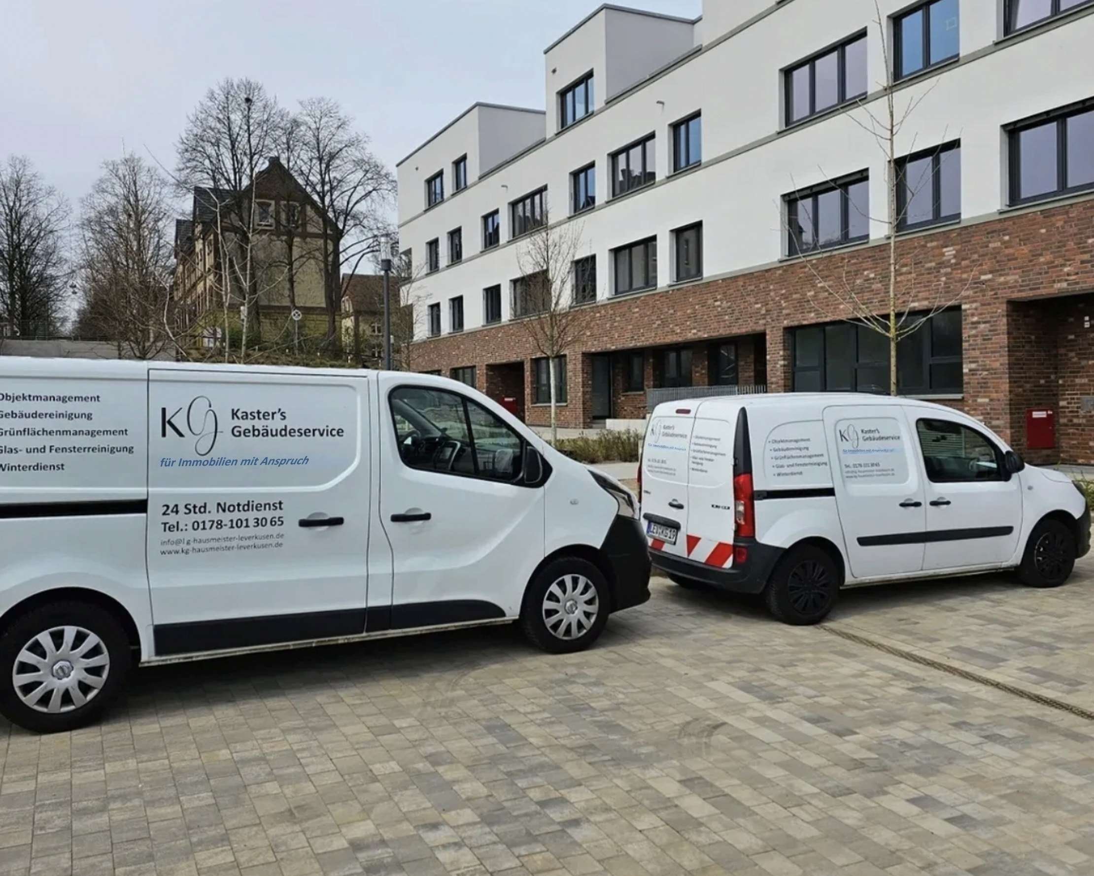 Die weißen Fahrzeuge von Kaster’s Gebäudeservice vor einer Wohnanlage
